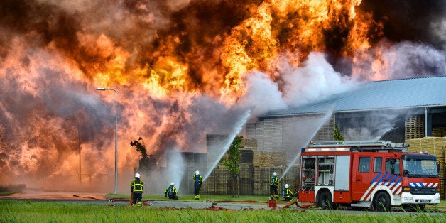 Fire fighters behind a fire engine trying to put out a fire in a factory and warehouse.