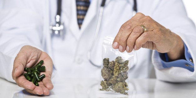 Unrecognizable male wearing lab coat and stethoscope holding pills and marijuana, isolated on white background, selective focus