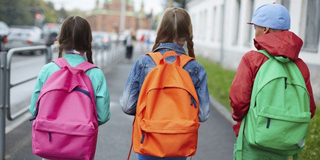 Backs of schoolkids with colorful rucksacks moving in the street
