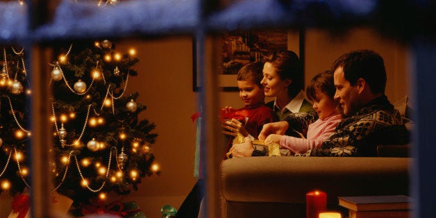 Family opening gifts on Christmas Eve, viewed through window