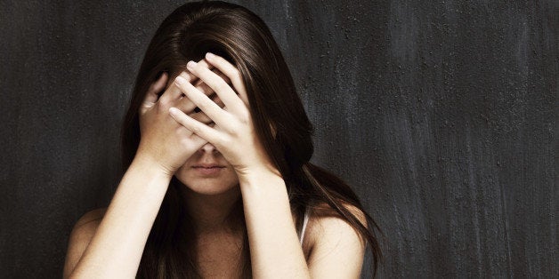 A studio shot of a sad young woman holding her head in her hands