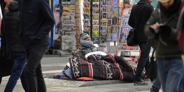 People walk past a homeless man sitting on the pavement in a street as temperatures plunged under 0 degrees Celsius (32 Fahrenheit) on January 26, 2017 in Lyon. / AFP / PHILIPPE DESMAZES (Photo credit should read PHILIPPE DESMAZES/AFP/Getty Images)