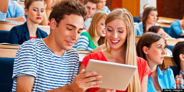 Large group of students sitting in the lecture hall at university. Focus on the young woman and man using a digital tablet to