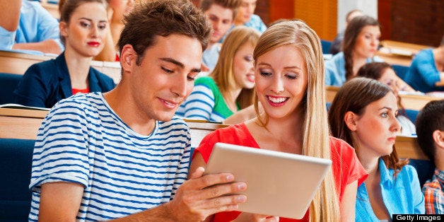 Large group of students sitting in the lecture hall at university. Focus on the young woman and man using a digital tablet together.