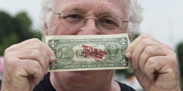 Ben Cohen, co-founder of Ben & Jerry's Ice Cream, holds up a one-dollar bill he stamped with the words 'Not to be used for bribing politicians' as he advocates to get money out of politics, outside Union Station in Washington on June 18, 2013. Cohen manned a stamping station to stamp people's money with the slogan and once people showed that their currency had been stamped, they received a free Ben & Jerry's ice cream cone. AFP PHOTO / Saul LOEB (Photo credit should read SAUL LOEB/AFP/Getty Images)