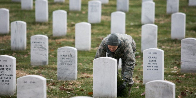 ARLINGTON, VA - DECEMBER 14: Army Tech Sgt. Danielle Williams, stationed at Fort Belvoir, lays a wreath at the foot of a headstone in Section 60 of Arlington National Cemetery, December 14, 2013 in Arlington, Virginia. Volunteers and families of the fallen placed thousands of remembrance wreaths on headstones throughout the cemetery on National Wreaths Across America Day. (Photo by Drew Angerer/Getty Images)