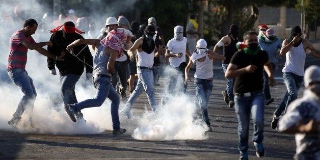 Palestinian protesters stand amid smoke after Israeli forces fired tear gas during clashes in Shuafat, East Jerusalem on July
