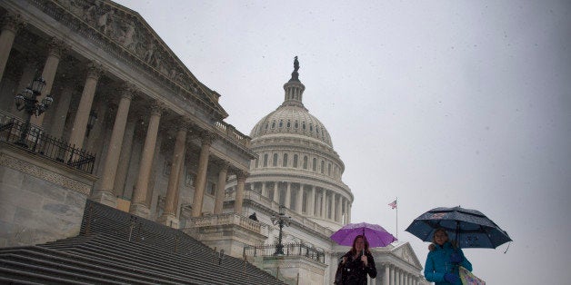 People hold umbrellas as they walk past the US Capitol Building in Washington, DC, December 10, 2013 just as it begins to snow. Fresh winter snow moved into the US mid-Atlantic region on Tuesday, shutting schools and offices in the nation's capital and elsewhere as the mid-section of the US remained in the grip of Arctic air that showed no signs of easing. AFP PHOTO / Jim WATSON (Photo credit should read JIM WATSON/AFP/Getty Images)