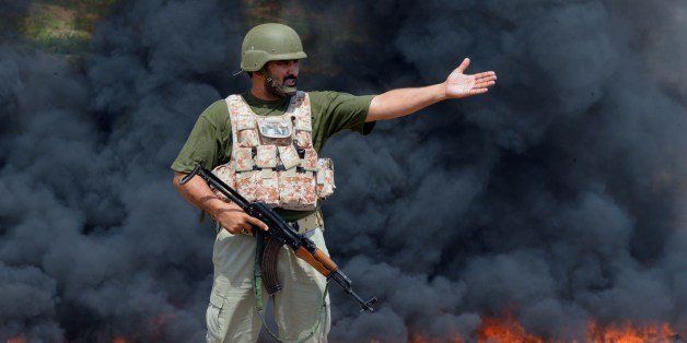 A Pakistani paramilitary soldier gestures as he stands guard beside a burning pile of seized drugs during a ceremony to mark International Day against Drug Abuse and Illicit Trafficking on the outskirts of Peshawar on June 26, 2014. Pakistan's war-torn neighbour Afghanistan is the world's largest producer of opium, the raw material for heroin. Efforts to cut production have failed in the 13 years since US-led forces toppled the Taliban regime there. More than 45 percent of Afghanistan's illicit opiates pass through Pakistan on their way to markets in Europe and Asia, according to the UN Office on Drugs and Crime. AFP PHOTO/A MAJEED (Photo credit should read A Majeed/AFP/Getty Images)