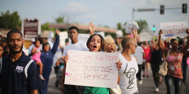 FERGUSON, MO - AUGUST 14: Demonstrators protest the shooting death of teenager Michael Brown on August 14, 2014 in Ferguson, Missouri. Brown was shot and killed by a Ferguson police officer on August 9. Police in Ferguson have changed their procedure for dealing with the protests after being chastised for a heavy-handed approach which has resulted in four days of violence. Today three police cars and four officers on foot led the way during a protest march. (Photo by Scott Olson/Getty Images)