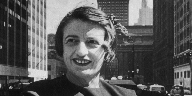 1957: Russian-born American author and philosopher Ayn Rand, smiles and stands outdoors with her arms folded, in front of th