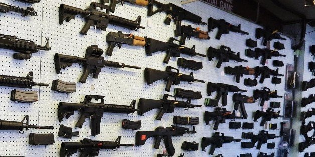 In this July 20, 2014 photo, with guns displayed for sale behind her, a gun store employee helps a customer at Dragonman's, east of Colorado Springs, Colo. When Colorado lawmakers expanded background checks on firearms last year, they were expecting a huge increase. But the actual number the first 12 months of the law is far lower than projected, according to an analysis of state data by The Associated Press. (AP Photo/Brennan Linsley)