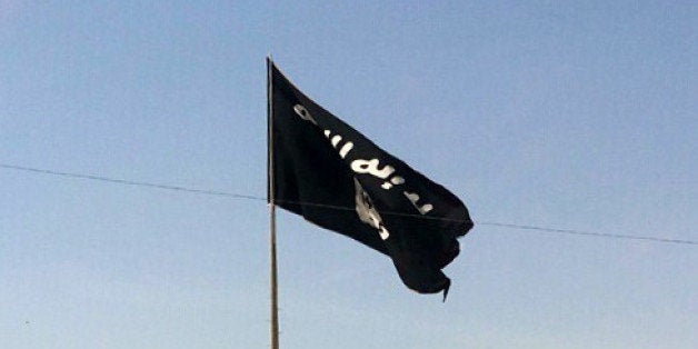 This Tuesday, July 22, 2014 photo shows a motorist passing by a flag of the Islamic State group in central Rawah, 175 miles (281 kilometers) northwest of Baghdad, Iraq, nearly six weeks since a Sunni militant blitz led by the Islamic State extremist group seized large swaths of northern and western Iraq. (AP Photo)