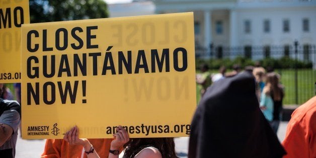 Protestors hold a sign and wear orange prisoners' jumpsuits as they call for the closing of the Guantanamo Bay detention faci