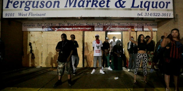 People stand in front of a convenience store after it was looted early Saturday, Aug. 16, 2014, in Ferguson, Mo. The violence stemmed from the shooting death of Michael Brown by police a week ago after the teen allegedly stole a box of cigars from the store. (AP Photo/Charlie Riedel)