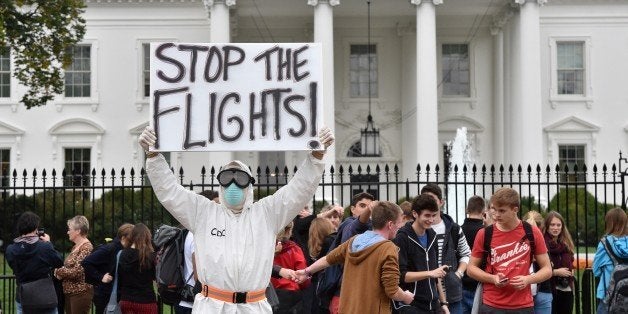 Jeff Hulbert from Annapolis, Maryland, dressed in a protective suit and mask holds a poster demanding for a halt of all flights from West Africa,as he protests outside the White House in Washington, DC on October 16, 2014. Top US health officials faced a grilling Thursday by lawmakers infuriated over the nation's fumbling response to the Ebola outbreak, as the Obama administration scrambles to contain the disease's spread. US authorities began screening for Ebola on Thursday at the Washington area Dulles airport, Chicago's O'Hare, Newark and Atlanta airports, after New York's JFK began screening last week.Together, the airports receive 94 percent of travelers from the Ebola-affected countries. AFP PHOTO/MLADEN ANTONOV (Photo credit should read MLADEN ANTONOV/AFP/Getty Images)