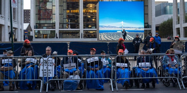People, some in wheelchairs, gather at Lincoln Center, with the Metropolitan Opera House in the background, as they protest "