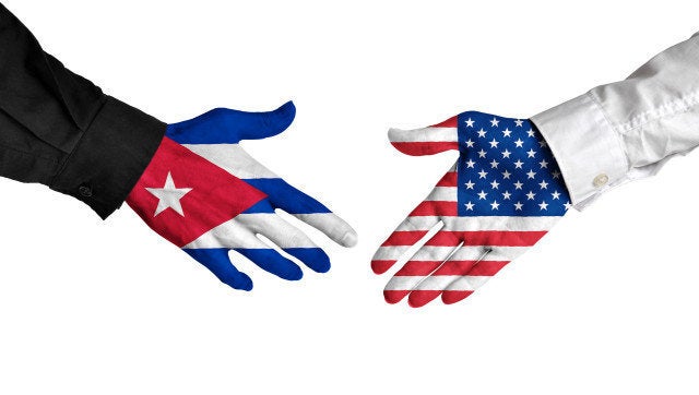 Diplomatic handshake between leaders from Cuba and the United States with flag-painted hands.