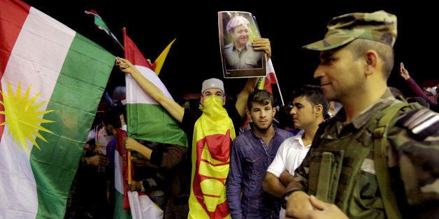 In this Tuesday, Oct. 28, 2014 photo, a supporter of Kurdish Peshmerga forces holds a large Kurdish flag and a poster of Iraq