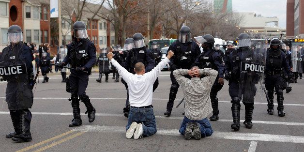 ST. LOUIS MO - NOVEMBER 30 : Two men who randomly joined demonstrators protesting the shooting death of Michael Brown kneel in the intersection as they confront police officers in riot gear November 30, 2014 in St. Louis, Missouri. Brown, a 18-year-old black male teenager was fatally wounded by Darren Wilson, a white Ferguson, Missouri Police officer on August 9, 2014. A St. Louis County 12-member grand jury who reviewed evidence related to the shooting decided not to indict Wilson with charges sparking riots through out Ferguson. (Photo by Joshua Lott/Getty Images)
