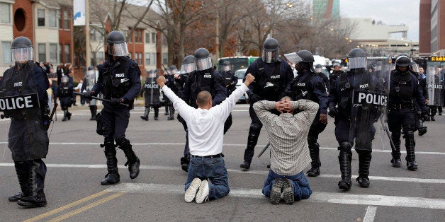 ST. LOUIS MO - NOVEMBER 30 : Two men who randomly joined demonstrators protesting the shooting death of Michael Brown kneel in the intersection as they confront police officers in riot gear November 30, 2014 in St. Louis, Missouri. Brown, a 18-year-old black male teenager was fatally wounded by Darren Wilson, a white Ferguson, Missouri Police officer on August 9, 2014. A St. Louis County 12-member grand jury who reviewed evidence related to the shooting decided not to indict Wilson with charges sparking riots through out Ferguson. (Photo by Joshua Lott/Getty Images)