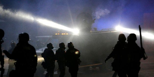 Police in riot gear stand around an armored vehicle as smoke fills the streets Tuesday, Nov. 25, 2014, in Ferguson, Mo. Missouri's governor ordered hundreds more state militia into Ferguson on Tuesday, after a night of protests and rioting over a grand jury's decision not to indict police officer Darren Wilson in the fatal shooting of Michael Brown, a case that has inflamed racial tensions in the U.S. (AP Photo/Charlie Riedel)