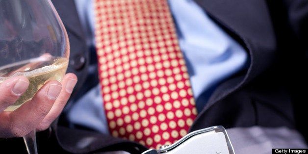 A businessman on a jet plane with fastened seat belt, an elegant suit and a glass of white wine. First class privileges.