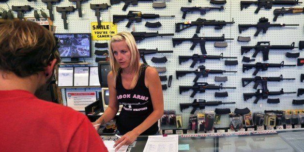 In this July 20, 2014 photo, with guns displayed for sale behind her, a gun store employee helps a customer at Dragonman's, east of Colorado Springs, Colo. When Colorado lawmakers expanded background checks on firearms last year, they were expecting a huge increase. But the actual number the first 12 months of the law is far lower than projected, according to an analysis of state data by The Associated Press. (AP Photo/Brennan Linsley)