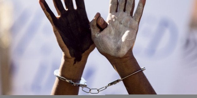 An African asylum seeker, who entered Israel illegally via Egypt, uses handcuffs and raises up his hands painted in black and