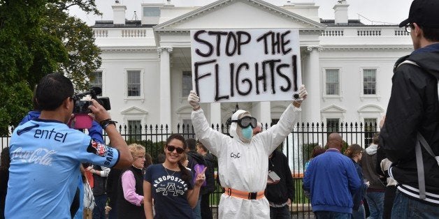 A tourist poses for a photo next to Jeff Hulbert from Annapolis, Maryland, dressed in a protective suit and mask demanding for a halt of all flights from West Africa, outside the White House in Washington, DC on October 16, 2014. Top US health officials faced a grilling Thursday by lawmakers infuriated over the nation's fumbling response to the Ebola outbreak, as the Obama administration scrambles to contain the disease's spread. Centers for Disease Control (CDC) director Thomas Frieden has become the most prominent target of the criticism, which has mounted as it emerged that a second Texas health care worker infected with the deadly disease was allowed to board a commercial flight despite reporting a low-grade fever. AFP PHOTO/MLADEN ANTONOV (Photo credit should read MLADEN ANTONOV/AFP/Getty Images)