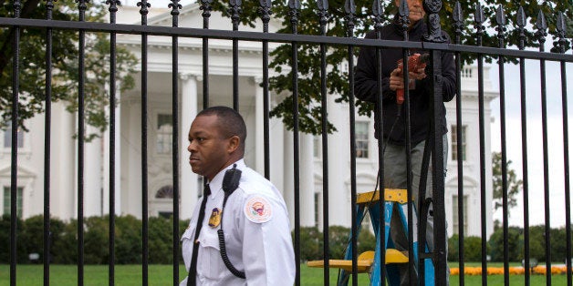 ** UPDATES THE CHARGES FILED AGAINST DOMINIC ADESANYA ** A Secret Service police officer walks outside the White House in Washington, Thursday, Oct. 23, 2014, as a maintenance worker performs fence repairs as part of a previous fence restoration project. Dominic Adesanya, the 23-year-old Maryland man who climbed over the White House fence was ordered held without bond in an appearance Thursday before a federal magistrate judge. He has been charged with unlawfully entering the restricted grounds of the White House and harming two police dogs. (AP Photo/Evan Vucci)