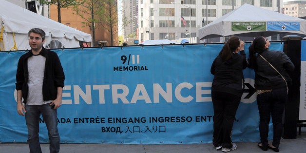 A visitor to the Sept. 11 Memorial, left, poses for a photo as others, right, peer at the entrance line, Saturday, May 4, 2013, in New York. Faced with hefty operating costs, the foundation building the underground 9/11 museum at the World Trade Center has decided to charge a mandatory admission fee of $20 to $25 when the site opens next year. Entry to the memorial plaza with its twin reflecting pools will still be free, but the decision to charge for the underground museum housing relics of the terror attacks has been greeted with dismay by some relatives of trade center victims. (AP Photo/Mary Altaffer)