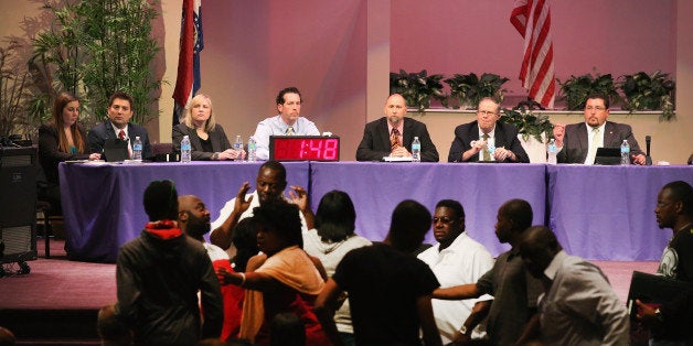 FERGUSON, MO - SEPTEMBER 09: Mayor James Knowles (seated R) ) and city council members wait until angry residents are calmed down during the Ferguson city council meeting on September 9, 2014 in Ferguson, Missouri. The meeting was held at Greater Grace Church to accommodate the large crowd. Most residents used the meeting to express their anger at how the police and city council handled the shooting of teenager Michael Brown and the unrest that followed. (Photo by Scott Olson/Getty Images)