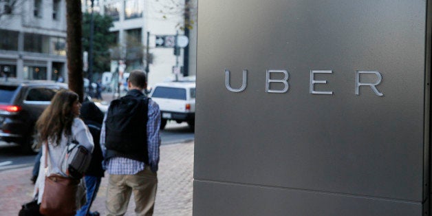 In this photo taken Tuesday, Dec. 16, 2014, a couple walks past the headquarters of Uber in San Francisco. (AP Photo/Eric Risberg)