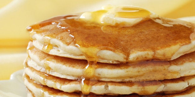 Golden pancakes with butter and warm maple syrup. Close-up with extremely shallow dof and soft yellow background.