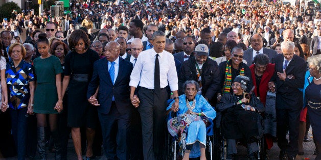 President Barack Obama, center, walks as he holds hands with Amelia Boynton Robinson, who was beaten during "Bloody Sunday," as they and the first family and others including Rep. John Lewis, D-Ga,, left of Obama, walk across the Edmund Pettus Bridge in Selma, Ala. for the 50th anniversary of âBloody Sunday," a landmark event of the civil rights movement, Saturday, March 7, 2015. From front left are Marian Robinson, Sasha Obama. first lady Michelle Obama. Obama, Boynton and Adelaide Sanford, also in wheelchair. (AP Photo/Jacquelyn Martin)