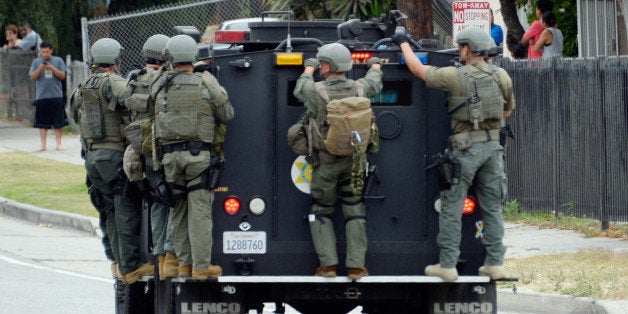 LOS ANGELES, CA - JUNE 25: Los Angeles County Sheriff's SWAT team members standing on a armored car arrive to help Los Angeles Police Department officers during a massive manhunt for a suspect who attempted to kill two detectives on June 25, 2013 in Los Angeles, California. The shooting happened in the early morning hours as the two detectives were ambushed and slightly injured outside the Los Angeles Police Department's Wilshire Station, prompting the closure of a 25-square-block area in the Mid-City section of Los Angeles. (Photo by Kevork Djansezian/Getty Images)