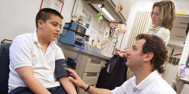 CICERO, IL - MAY 11: Stephen Egert, a registered nurse with the Pediatric Mobile Health Unit of Loyola University Medical Center, checks the blood pressure of fourth-grader Gerardo Gonzalez as he performs a physical exam for incoming fifth-graders outside David Burnham Elementary School May 11, 2004 in Cicero, Illinois. Assisting Egert is nurse practitioner Susan Finn. The Pediatric Mobile Health Unit, the first if its kind in the world, is a 40-foot long truck which accommodates two patient examination rooms, a laboratory, a medical records area and hearing booth. Since 1998 more than 50,000 uninsured and underinsured children in the Chicago area have been evaluated and treated at the unit. (Photo by Tim Boyle/Getty Images)