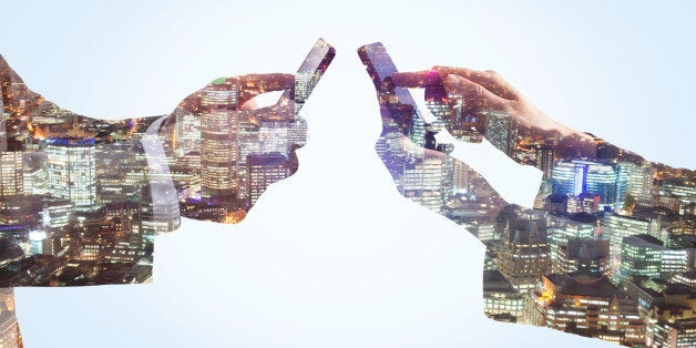 Double exposure of a business man and business woman communicating with smart phones with a view of the financial district of The City of London at night.