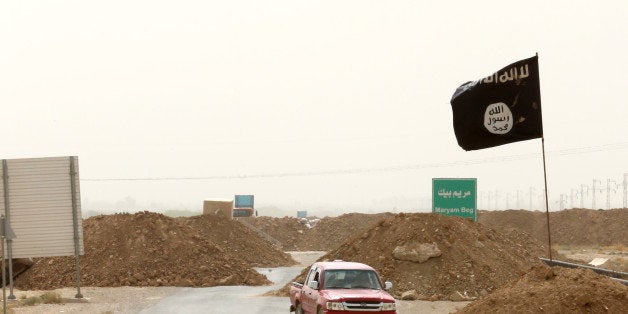 Islamic State militants pass a checkpoint bearing the group's trademark black flag in the village of Maryam Begg in Kirkuk, 290 kilometers (180 miles) north of Baghdad, Iraq, Monday, Sept. 29, 2014. (AP Photo/Hadi Mizban)