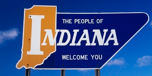 This is a road sign that says the people of Indiana welcome you. It is a welcome to Indiana road sign against a blue sky.