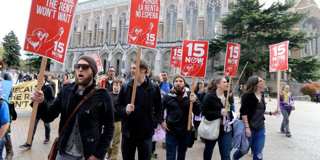 Students and other supporters protest, Wednesday, April 1, 2015, on the University of Washington campus in Seattle, in support of raising the minimum wage for campus workers to $15 an hour. Seattle's new $15 minimum wage law began going into effect Wednesday with a program to gradually raise wages through 2017 and beyond, but UW officials have questioned whether their status as a state entity would require them to raise wages for students and other campus workers on the same schedule. (AP Photo/Ted S. Warren)