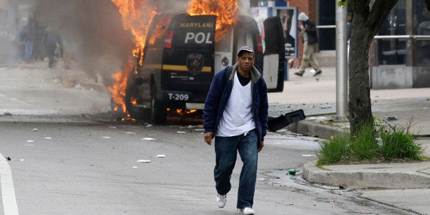 A man walks past a burning police vehicle, Monday, April 27, 2015, during unrest following the funeral of Freddie Gray in Bal