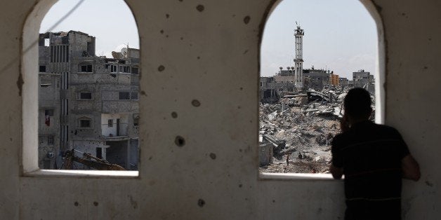 A man watches from an open window as Palestinian workers clear the rubble of destroyed buildings on April 15, 2015 in the eastern Gaza City neighborhood of Shejaiya which was heavily targeted during the 50-day war between Israel and Hamas militants in the summer of 2014. AFP PHOTO / THOMAS COEX (Photo credit should read THOMAS COEX/AFP/Getty Images)