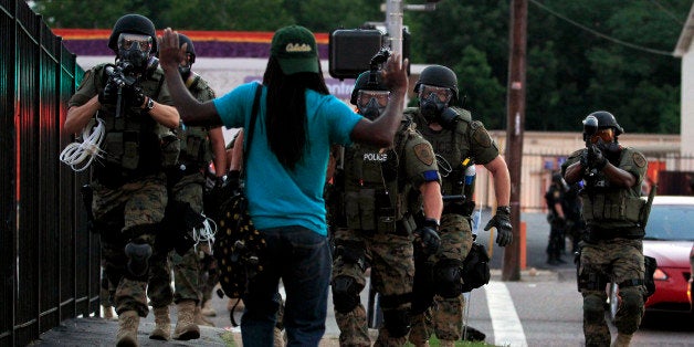 FILE - In this Aug. 11, 2014, file photo, police wearing riot gear walk toward a man with his hands raised in Ferguson, Mo. T