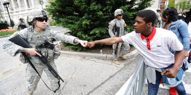 Brandon Payton, right, of Baltimore, fist-bumps a National Guardsman standing outside of City Hall as protesters march by to demonstrate the police-custody death of Freddie Gray, Thursday, April 30, 2015, in Baltimore. Baltimore police say they have turned over their criminal investigation to a prosecutor who will decide whether charges are warranted in the death of Gray. (AP Photo/David Goldman)