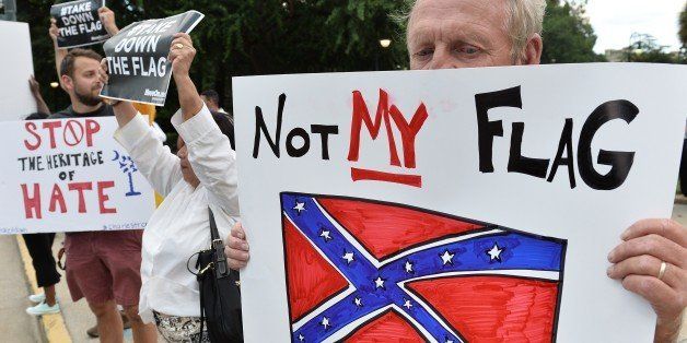 A man holds a sign up during a protest rally against the Confederate flag in Columbia, South Carolina on June 20, 2015. The racially divisive Confederate battle flag flew at full-mast despite others flying at half-staff in South Carolina after the killing of nine black people in an historic African-American church in Charleston on June 17. Dylann Roof, the 21-year-old white male suspected of carrying out the Emanuel African Episcopal Methodist Church bloodbath, was one of many southern Americans who identified with the 13-star saltire in red, white and blue. AFP PHOTO/MLADEN ANTONOV (Photo credit should read MLADEN ANTONOV/AFP/Getty Images)