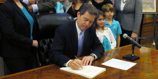 Kansas Gov. Sam Brownback signs a sweeping anti-abortion bill into law during a Statehouse ceremony, Friday, April 19, 2013, in Topeka, Kan. He is surrounded by legislators, abortion opponents and the family of Michael Schuttloffel, to the left just behind Brownback, a lobbyist for the Kansas Catholic Conference. (AP Photo/John Hanna)