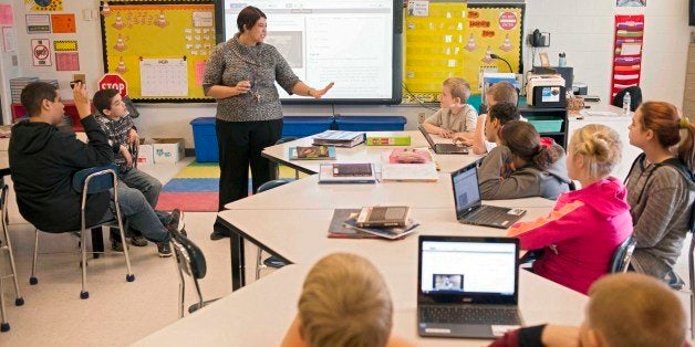 In this photo taken Feb. 12, 2015, sixth grade teacher Carrie Young guides her students through an exercise on their laptops