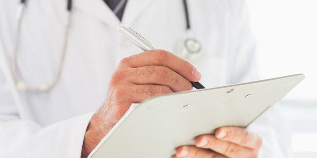 Midsection of male doctor writing on clipboard in hospital